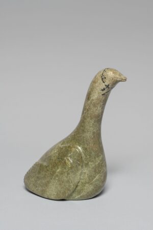 Stone carving of a loon, shown in profile with a smooth, rounded form and minimal detail. The bird’s head is slightly tilted, and simple incised lines define the eyes and wing, with natural stone veining adding texture.